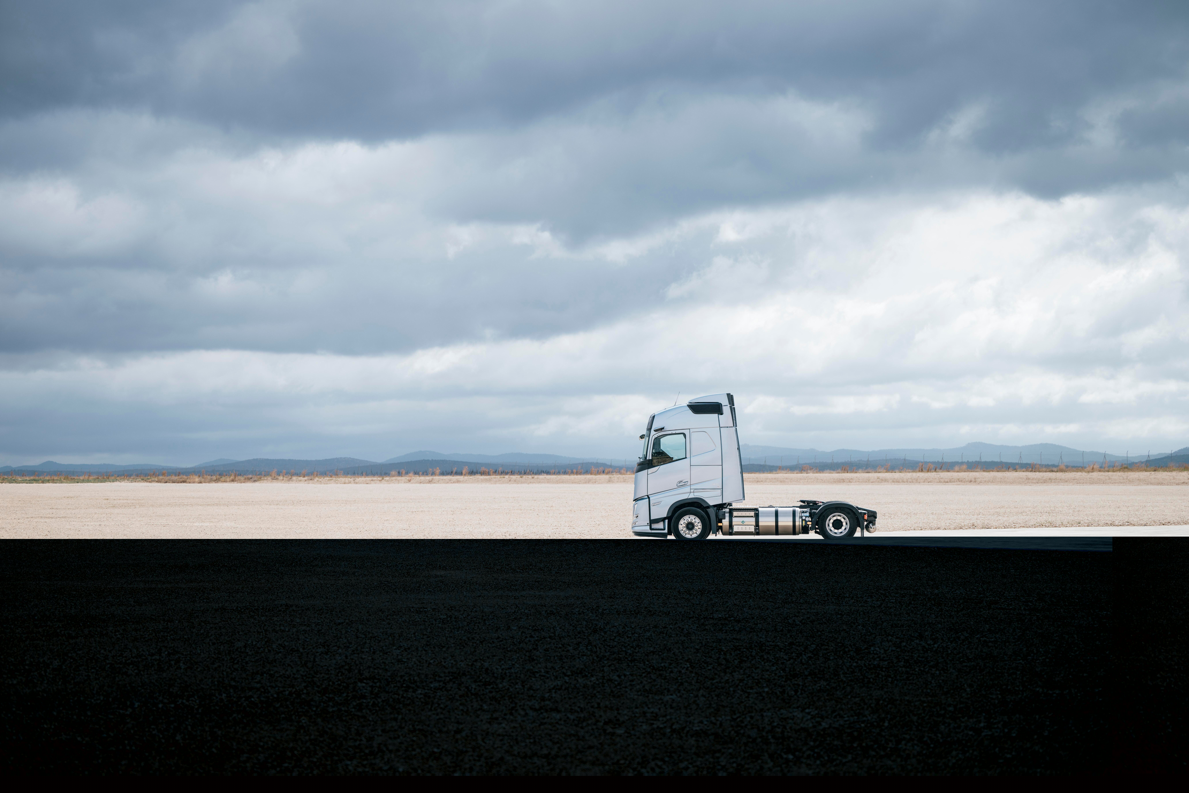 Vista laterale di un camion Volvo parcheggiato in un ampio spazio aperto sotto un cielo nuvoloso, con un paesaggio esteso e pochi elementi sullo sfondo.